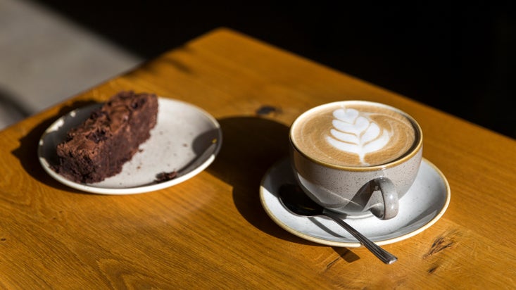 A piece of chocolate cake and a cup of coffee on a sunlit table